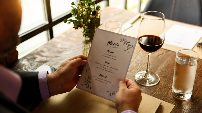 Man holding restaurant menu with a glass of red wine on the table