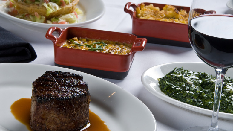 Steakhouse dinner with sides in the background including mac n cheese, creamed spinach, and vegetables