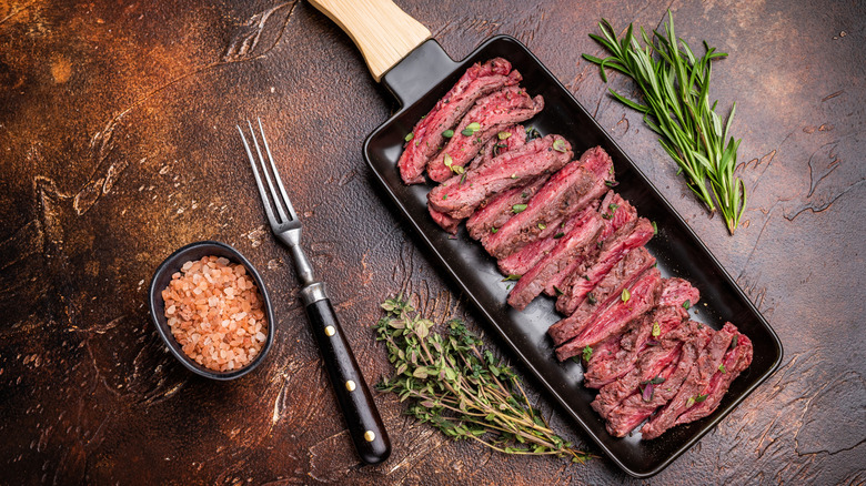 Grilled flank steak in a pan surrounded by herbs and spices