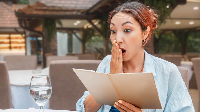 Woman looking shocked while reading restaurant menu
