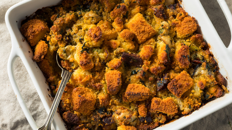 cornbread dressing in a white baking dish with a serving spoon stuck into it
