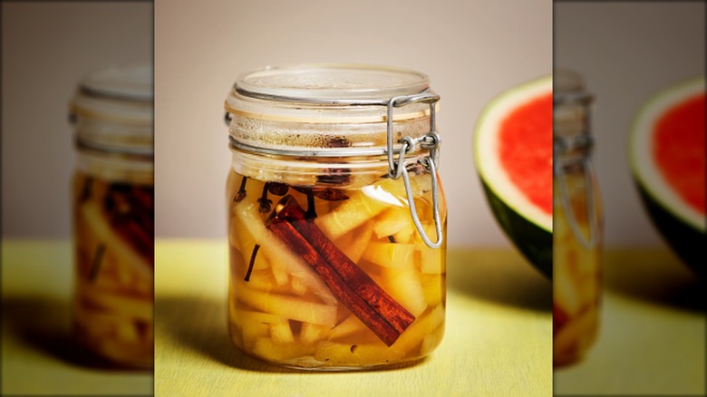 jar of pickled watermelon rind with half of a watermelon in the background