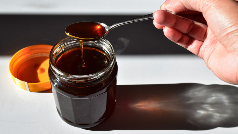 a hand spooning sorghum syrup from a glass jar