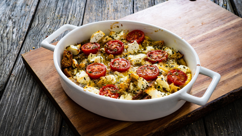 a tomato and bread casserole in a white dish on a wood board