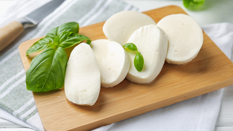 Slices of fresh mozzarella on a wooden cutting board with fresh basil