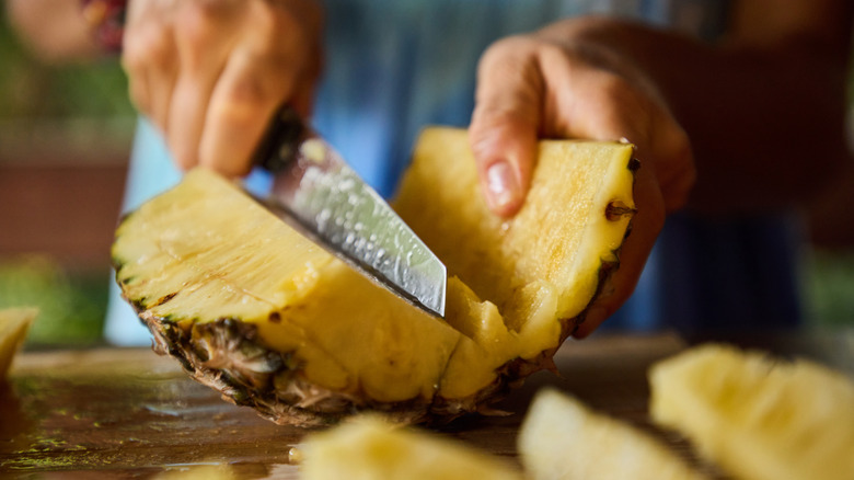 Close up of a person's hands chopping up a pineapple