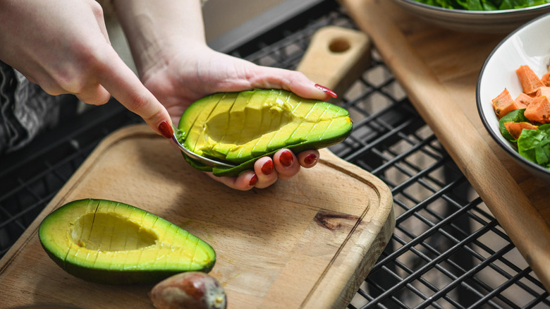 A woman's hands using a spoon to scrape out avocado slices