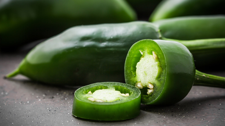 A sliced jalapeño in front of some whole jalapeños