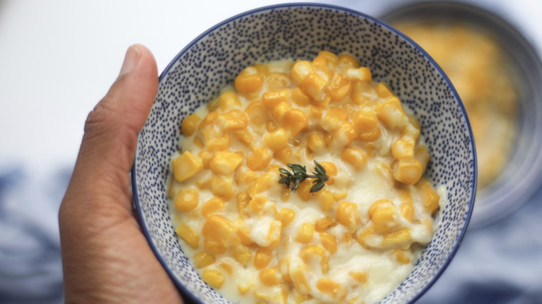 Hand holding blue and white bowl filled with Creamed Corn
