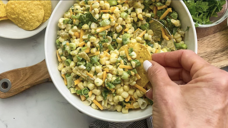 Hand dipping corn chip into Creamy Corn Dip