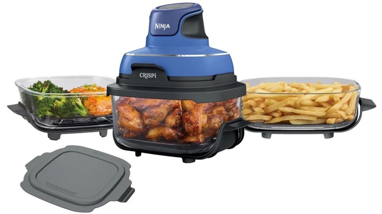 Glass air fryer cooking chicken surrounded by glass containers with vegetables and fries.