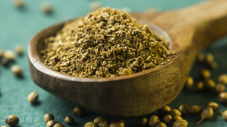 Ground coriander in a spoon with coriander seeds around it