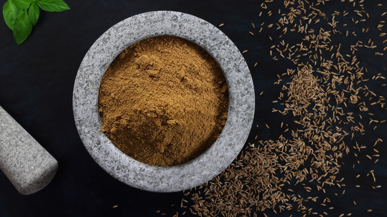 Mortar and pestle with ground cumin and cumin seeds around it