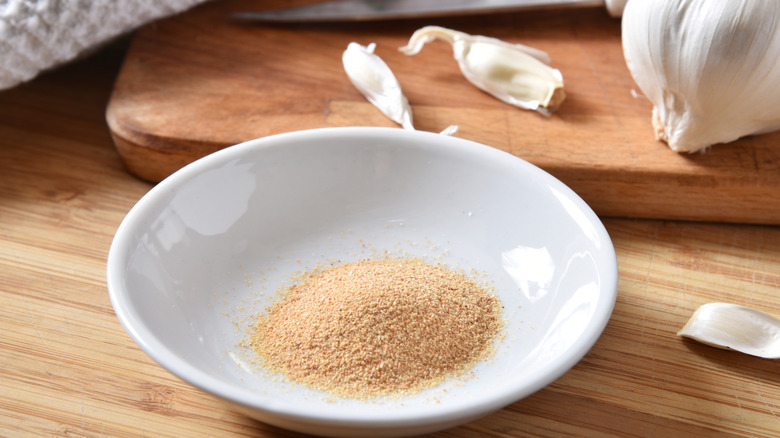 Bowl of garlic powder on wooden table with garlic in the background