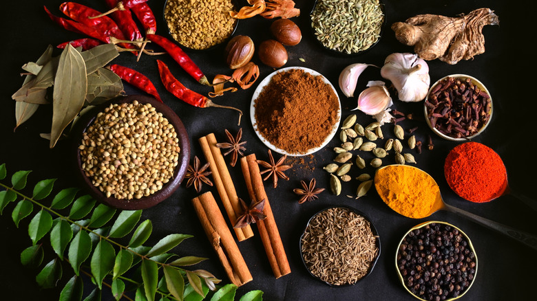 Top view of a variety of powdered and whole spices, including bay leaf, ginger, chili peppers, and cinnamon