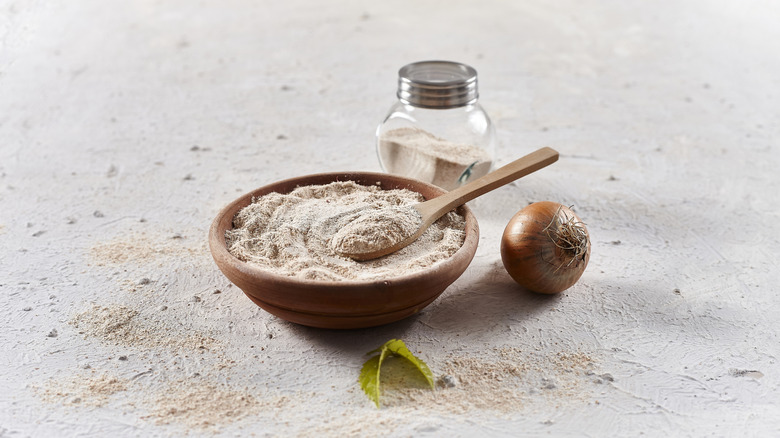Bowl of onion powder with small onion and jar of onion powder next to it