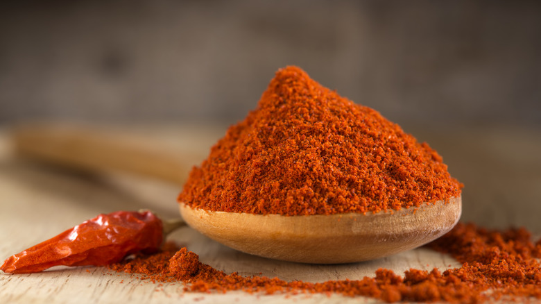 Spoon of paprika on wooden table next to one dried red pepper