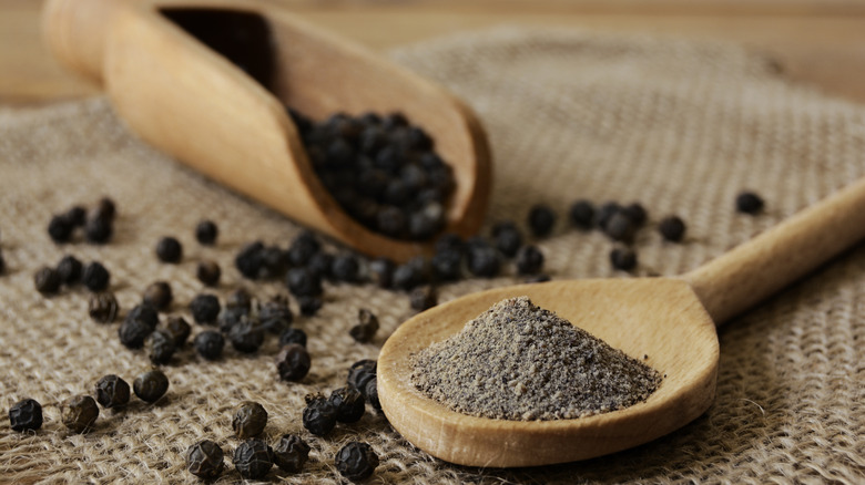 Whole peppercorns and ground pepper in wooden serving spoons on burlap
