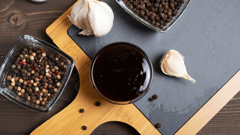 Bowl of thick teriyaki sauce surrounded by black peppercorns and garlic