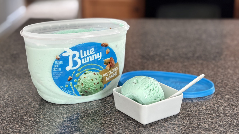 carton of pistachio almond ice cream with a scoop of ice cream in a dish