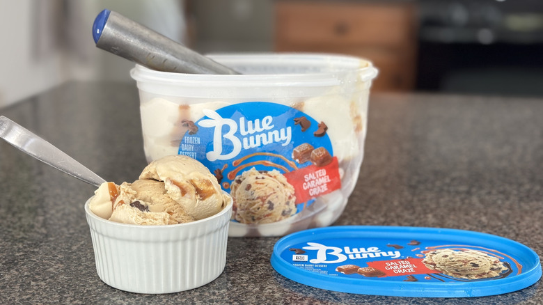 bowl of salted caramel ice cream scoops with carton and ice cream scoop in background