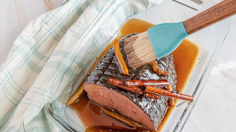 Whiskey glaze brushed onto baked ham with cinnamon sticks