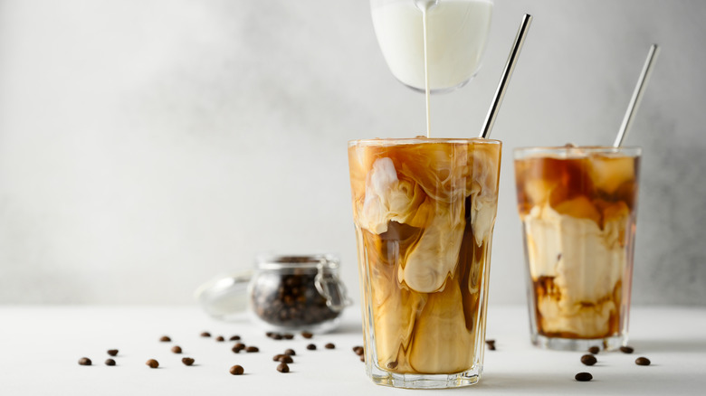 Milk being poured into a glass of iced coffee