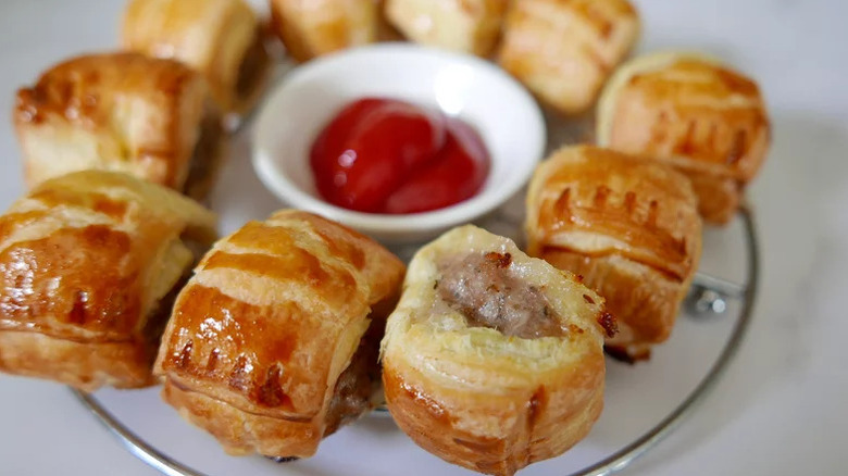 easy mini sausage rolls arranged in a circle on a serving plate with a small container of ketchup in the middle