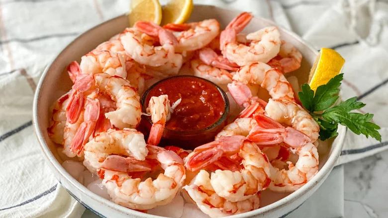 shrimp arranged in a circle inside a serving bowl with cocktail sauce in the middle and lemon wedges scattered around