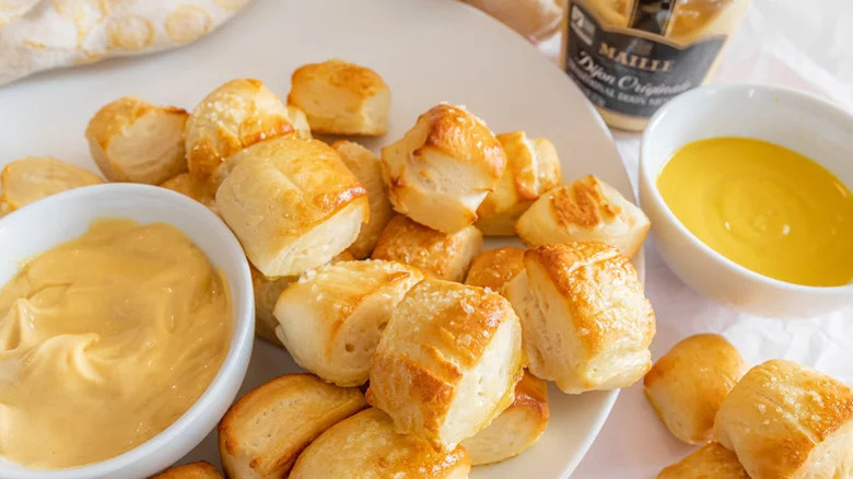 Homemade soft pretzel bites piled onto a plate with bowl of dijon mustard and another bowl of cheese sauce to the side