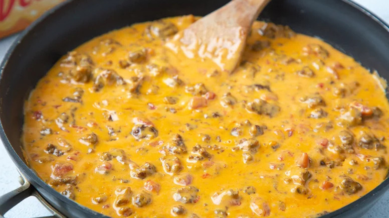 close up of Meaty Rotel queso dip in a skillet with a wooden spoon