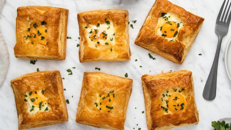 Puff pastry squares holding eggs and herbs.