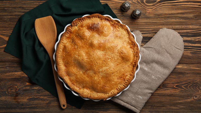 baked pie with wooden spatula and oven glove