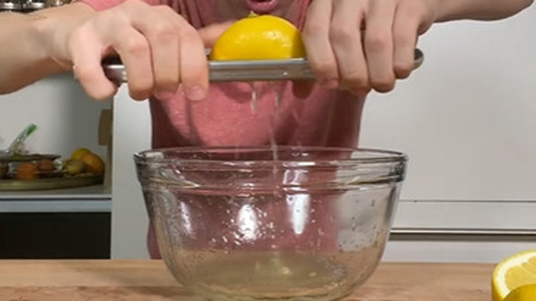 squeezing lemon with kitchen tongs into bowl