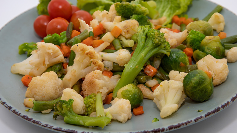 Broccoli, cauliflower, Brussels sprouts, cherry tomatoes, and diced carrots in a blue plate