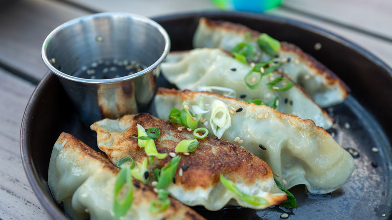 Crispy dumplings garnished with scallions and a small cup of soy sauce and sesame seed dip, all placed in a black plate