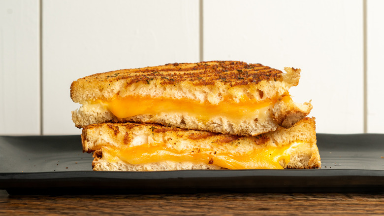 Two grilled cheese sandwiches with melty cheese on a black serving plate