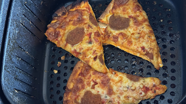 Three slices of pepperoni pizza inside an air fryer, freshly reheated