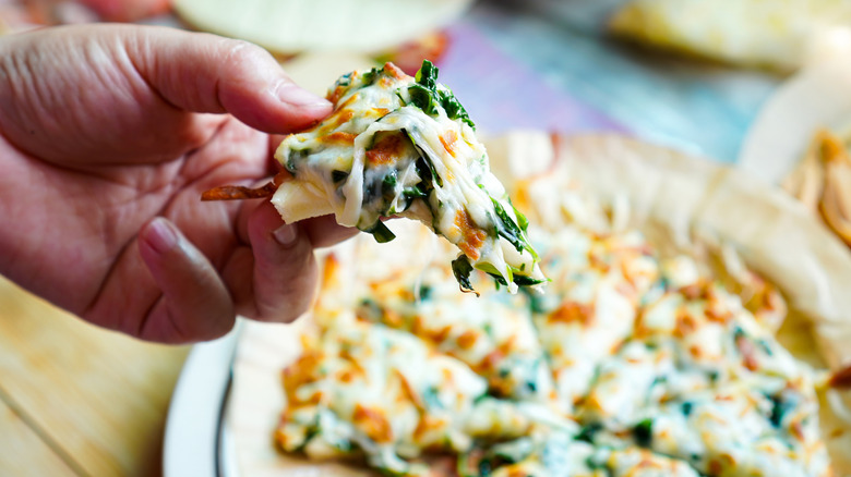 A hand holding up a slice of quiche