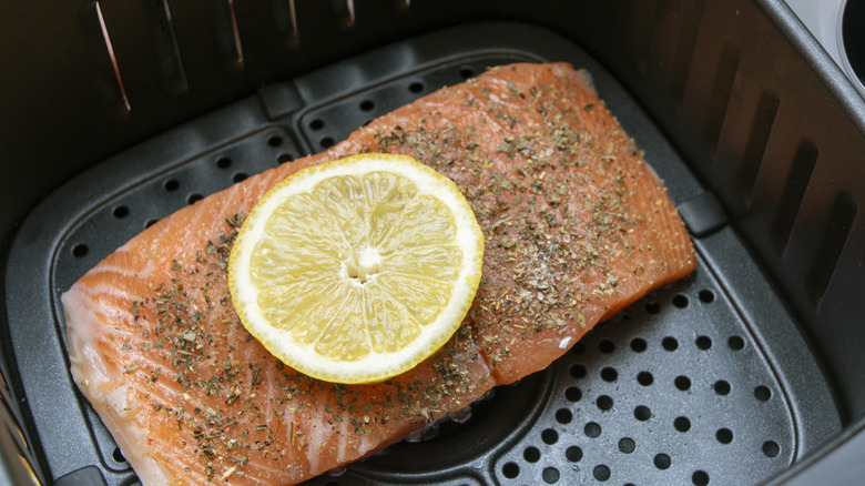 Seasoned salmon and a slice of lemon inside an air fryer basket