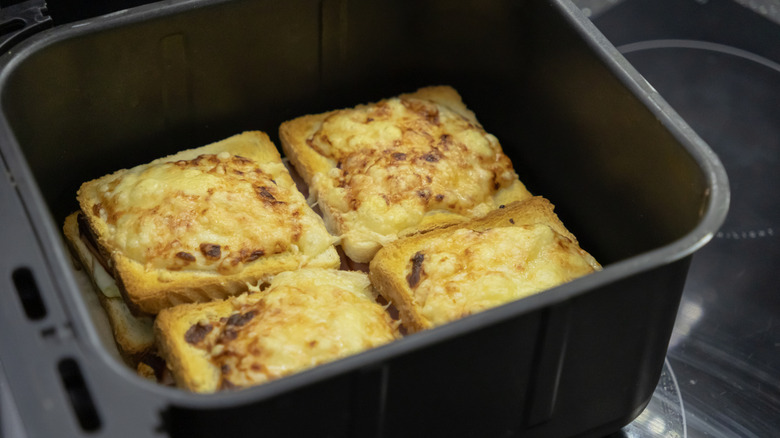 Four sandwiches with melted cheese on top, inside an air fryer basket