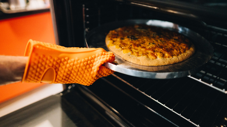Hand wearing oven mitt taking pizza out of oven.