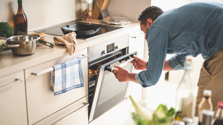 Person in denim shirt checking on food in electric oven.