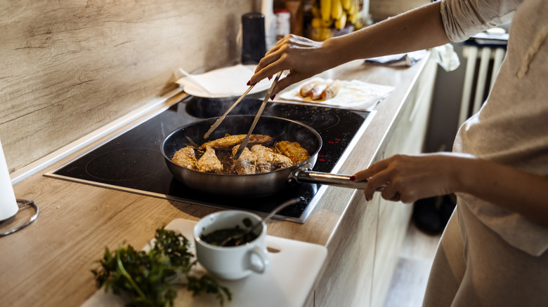Person cooking fish on an electric stovetop.