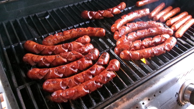 Scored hot dogs cooking on a grill
