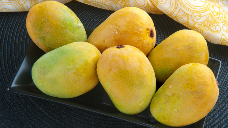Ripe mangoes on rectangular black plate.