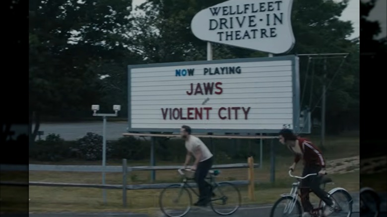 "Tony" scene showing two men biking past an old drive-in theater marquee.