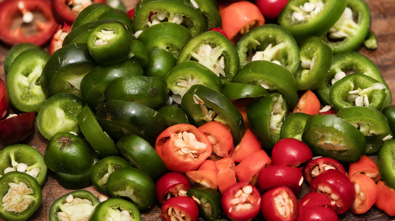 Red and green cut jalapeños on a wooden cutting board