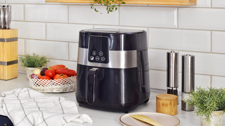 An air fryer on a kitchen counter surrounded by cutlery, spices, and other items.