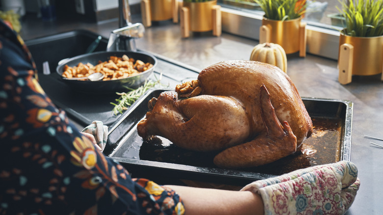 person with oven mitts taking turkey from oven